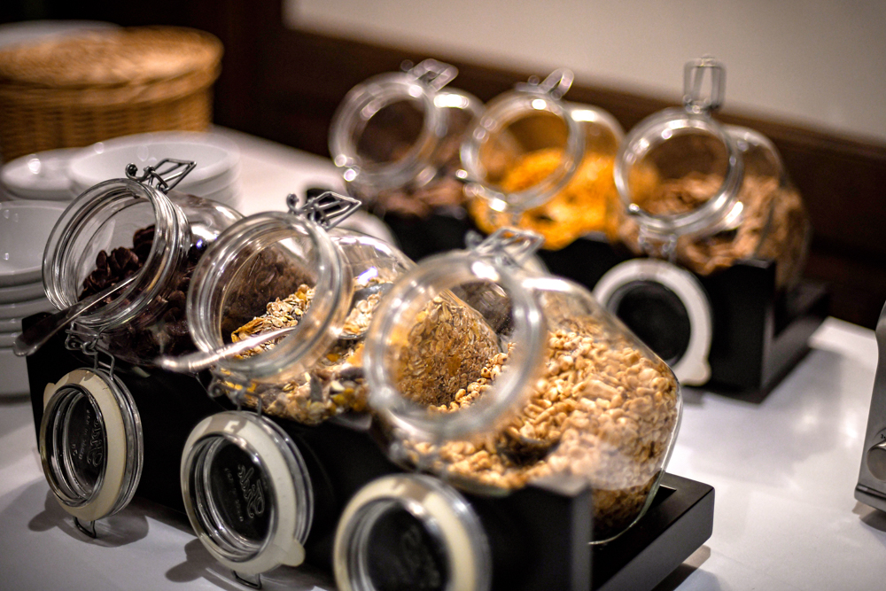 Verschiedene Müslisorten und Cerealien zur Auswahl in offenen Glasbehältern an einem Frühstücksbuffet.