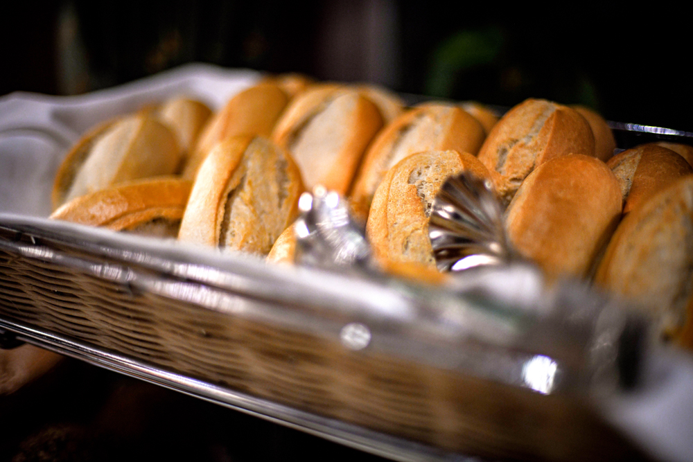 Nahaufnahme eines Korbes mit frisch aufgeschnittenen Brötchen und einer Servierzange auf einem Buffet.