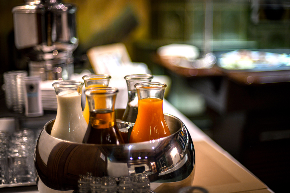 Verschiedene Säfte und Milch in Glaskaraffen in einem Kühler an einem Frühstücksbuffet.