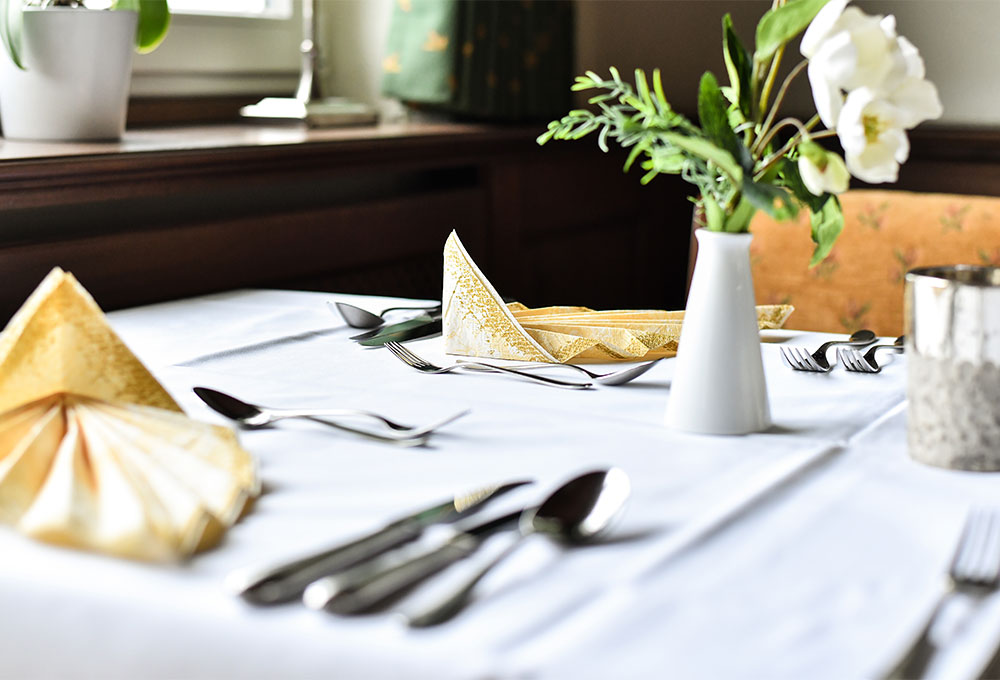 Elegant gedeckter Restauranttisch mit weißer Tischdecke, Besteck, gefalteten Servietten und einer kleinen Blumenvase.
